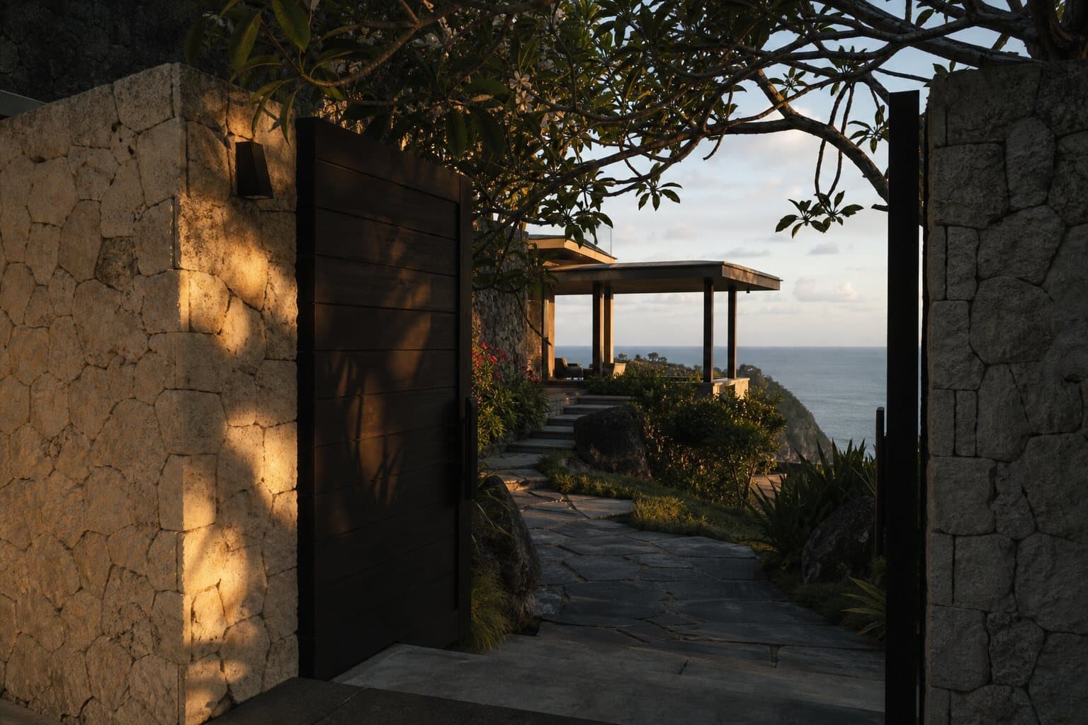The teak entrance gate of a cliffside villa in late afternoon light